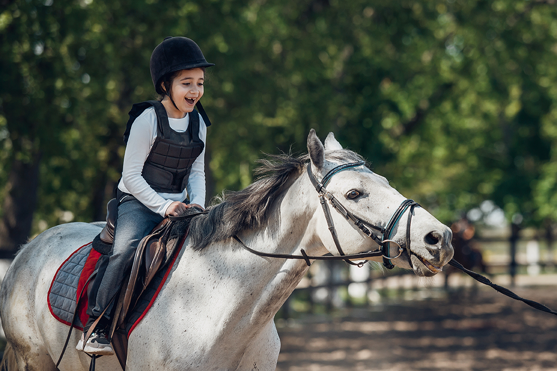 Smiling Little Girl in helmet Learning Horseback Riding. Instructor teaches kid Equestrian.